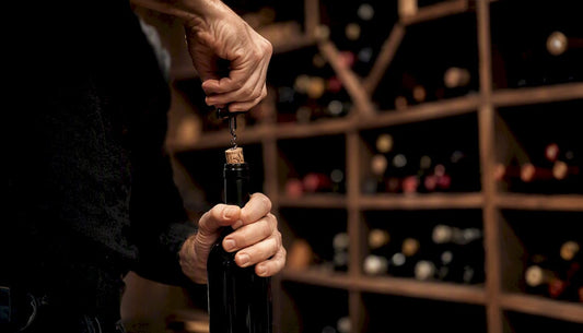 Hand uncorking wine bottle in cellar