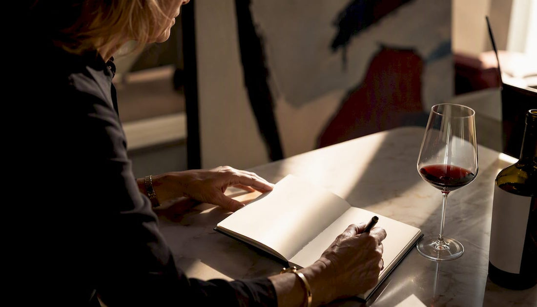 Hands writing wine journal with glass of red wine