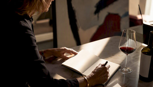 Hands writing wine journal with glass of red wine